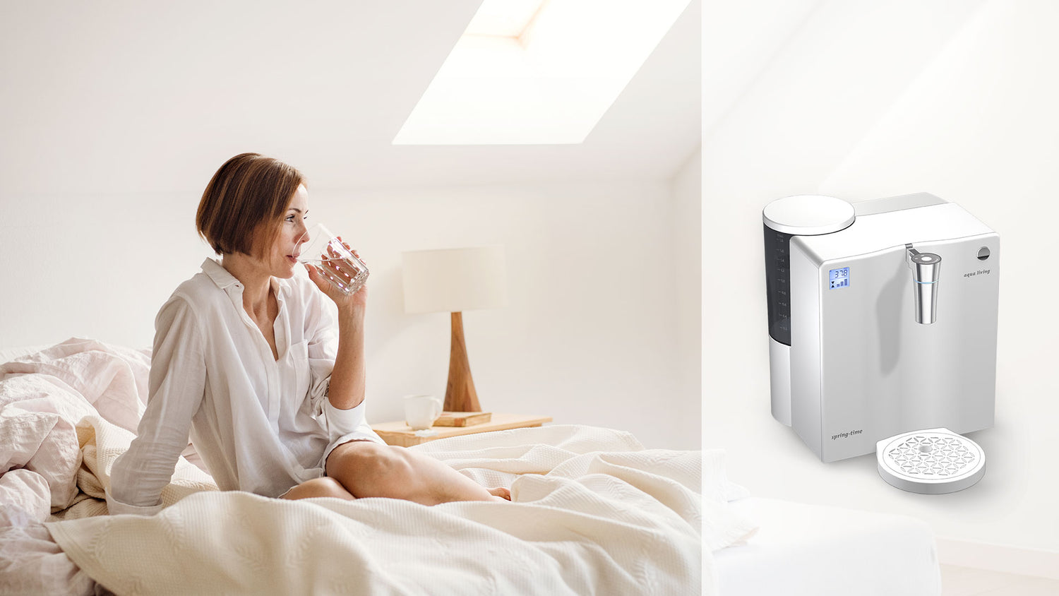 Wasseraufbereitung - eine gesundaussehende mittelalte Frau im weissen Nachthemd sitzt auf den Arm gestützt auf ihrem Bett und trinkt ein Glas rein gefiltertes Wasser, rechts im Bild, etwas hervorgehoben, ist ein Beispielprodukt für einen Wasserfilter zu sehen 