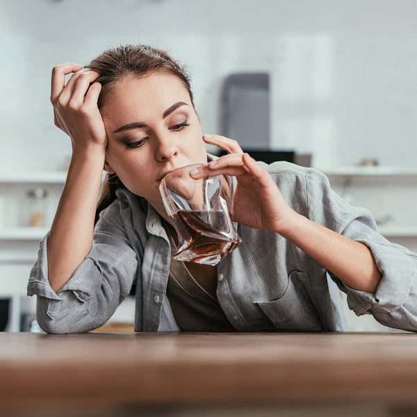 thema umgang-mit-alkohol - man sieht eine frustrierte junge frau an der küchentheke, die in ein glas mit cola und rum hineinschaut, sie stützt sich den kopf mit der anderen hand